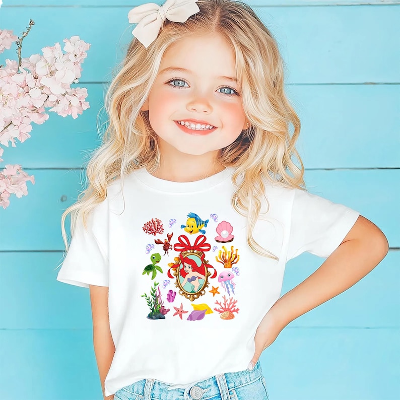 A young girl with blonde hair is smiling and wearing a white t-shirt with a colorful graphic of underwater sea creatures.