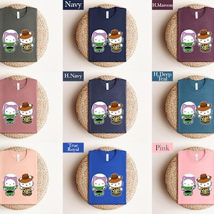 The image is a collage of nine t-shirts, each with a different color and design, arranged in a 3x3 grid. The t-shirts feature cartoon characters and are displayed on a woven mat.