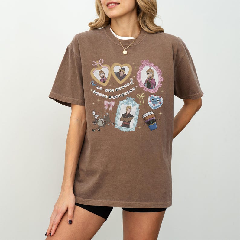 A woman wearing a brown t-shirt with various cartoon-style illustrations and text on it.