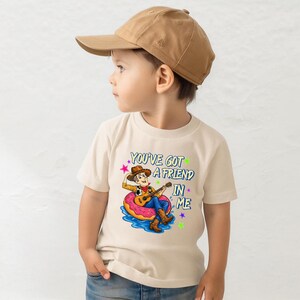 A young boy wearing a baseball cap and a t-shirt with a cartoon character and text printed on it.