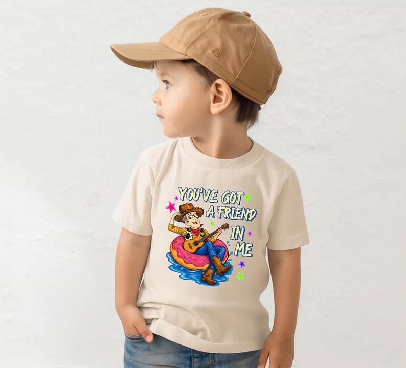 A young boy wearing a baseball cap and a t-shirt with a cartoon character and text printed on it.