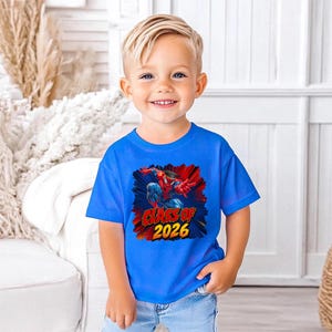 A young boy wearing a blue t-shirt with a graphic design and text, smiling at the camera.