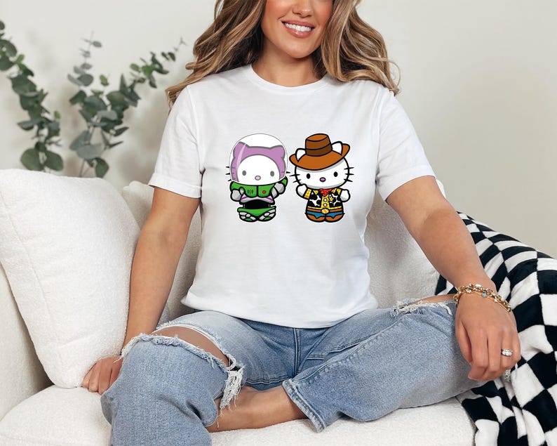 A woman wearing a white t-shirt with two cartoon characters, one wearing a green outfit and the other a cowboy hat, sitting on a couch.