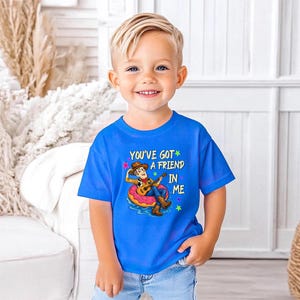 A young boy wearing a blue t-shirt with a cartoon character and text, smiling at the camera.