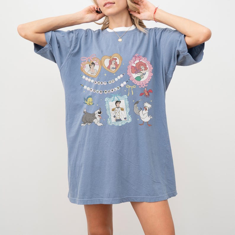 A woman wearing a blue t-shirt with a graphic design featuring various cartoon characters and text.