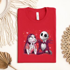 A red t-shirt with a graphic of two cartoon characters, a skeleton and a woman, sitting together.
