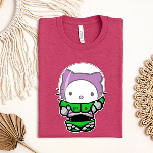 a pink t-shirt with a cartoon cat wearing a green spacesuit, along with some decorative elements such as a fan, a woven mat, and a string.