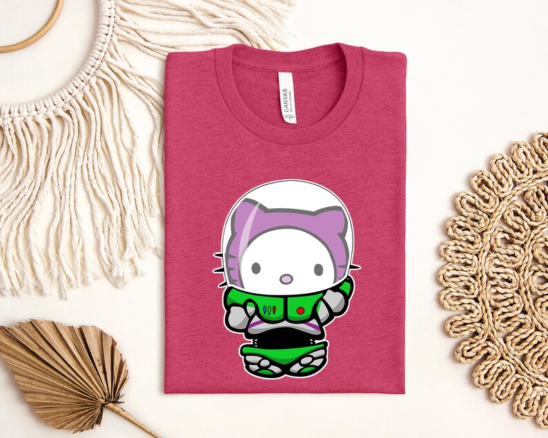 a pink t-shirt with a cartoon cat wearing a green spacesuit, along with some decorative elements such as a fan, a woven mat, and a string.