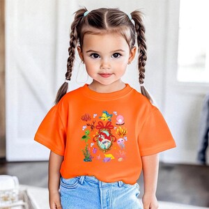 A young girl with pigtails wearing an orange t-shirt with a Disney character design.