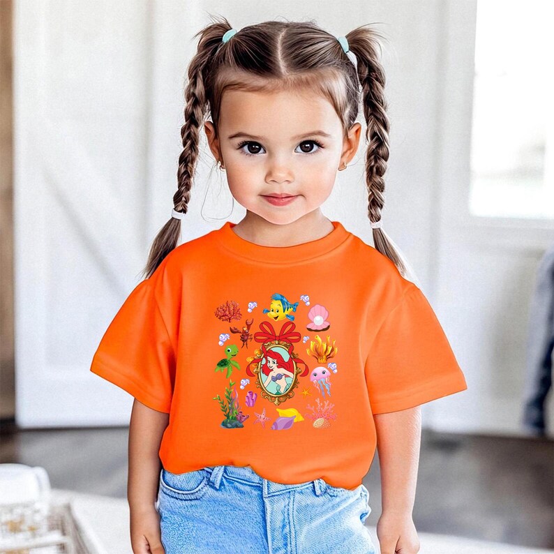 A young girl with pigtails wearing an orange t-shirt with a Disney character design.