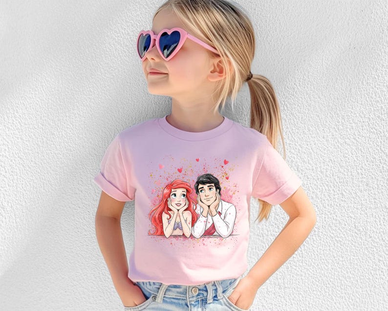 A young girl wearing a pink t-shirt with a cartoon image of two characters, one with red hair and the other with blonde hair, smiling and looking up at each other.