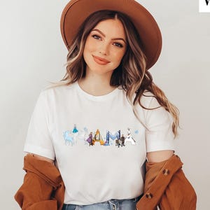 A woman wearing a white t-shirt with a graphic design and a brown hat, smiling at the camera.