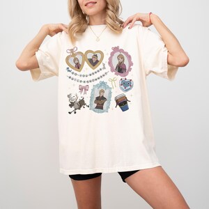 A woman wearing a white t-shirt with various cartoon-style illustrations and text on it.