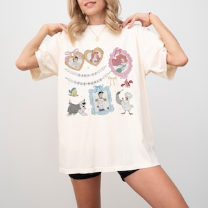 A woman wearing a white t-shirt with various cartoon characters and text printed on it.