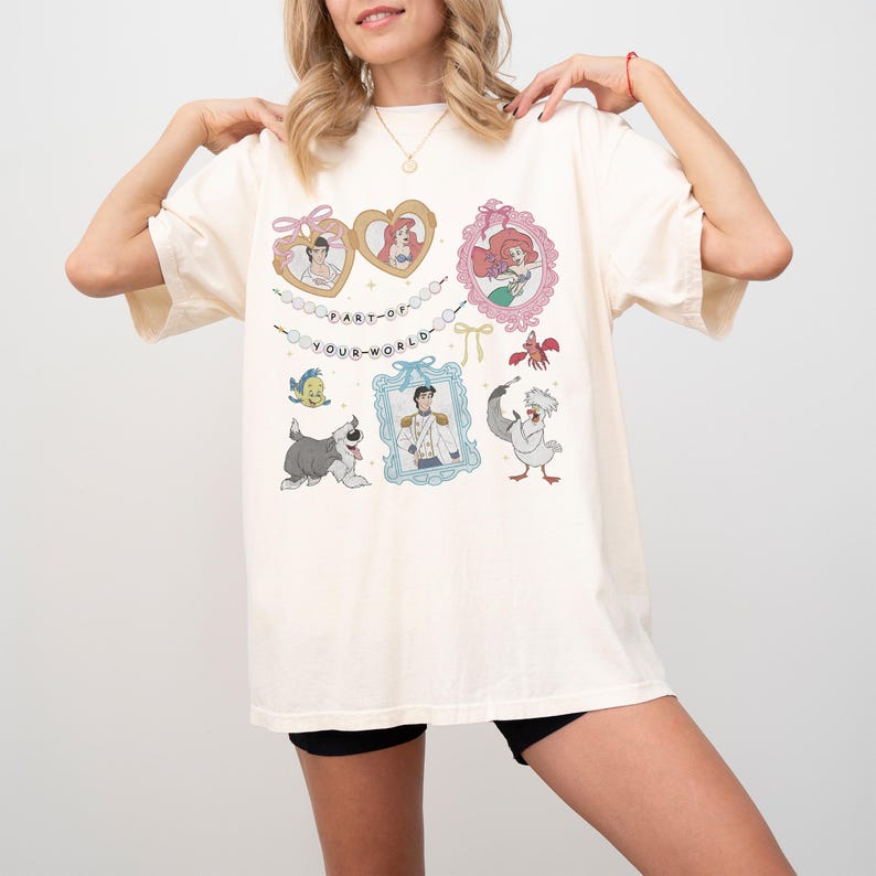 A woman wearing a white t-shirt with various cartoon characters and text printed on it.