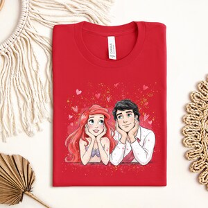 a red t-shirt with a drawing of two cartoon characters, a man and a woman, sitting together and smiling.