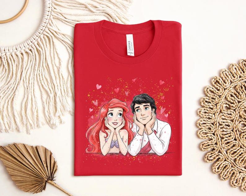 a red t-shirt with a drawing of two cartoon characters, a man and a woman, sitting together and smiling.