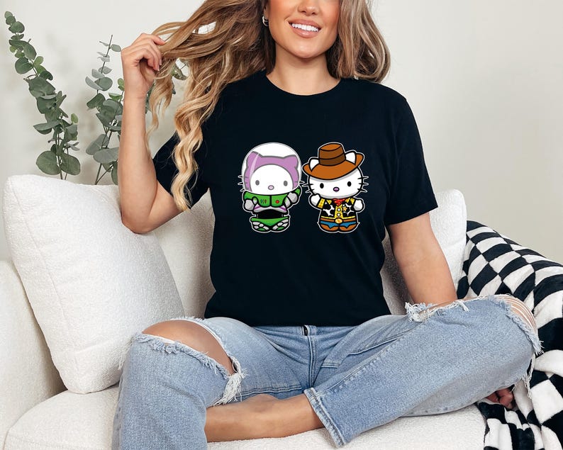 A woman sitting on a couch wearing a black t-shirt with a graphic of two cartoon characters, one wearing a green outfit and the other a cowboy hat.