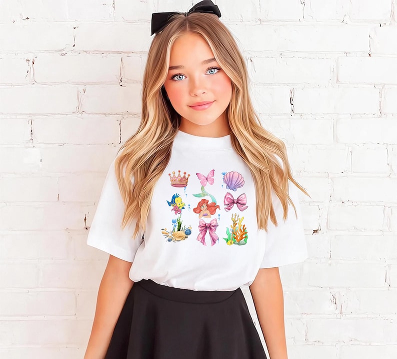 A young girl with long blonde hair wearing a white t-shirt with a colorful graphic design featuring characters from the Disney movie "The Little Mermaid".