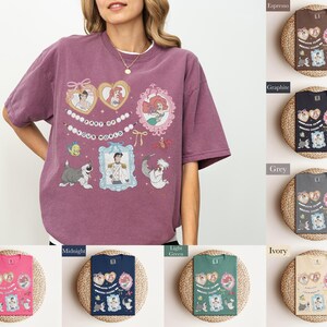 A woman wearing a purple t-shirt with various cartoon characters and designs, including a mermaid, a dog, and other whimsical elements.