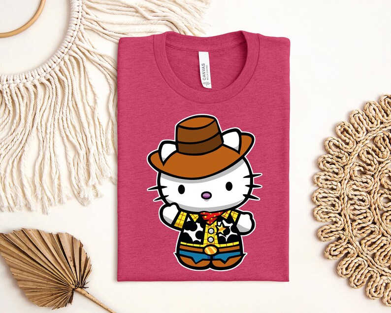 A pink t-shirt with a cartoon image of a cat wearing a cowboy hat and a yellow and blue outfit, along with a straw hat and a woven mat.