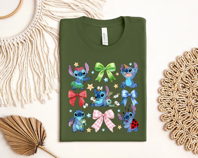 a green t-shirt with a colorful design of cartoon characters, including Stitch, a blue bunny, and other whimsical elements. The t-shirt is displayed on a white background, surrounded by various decorative items such as a woven basket, a leaf, and a star.