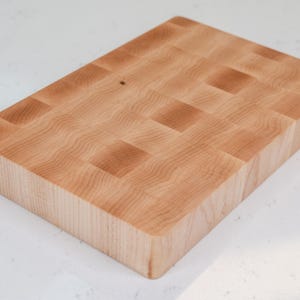 Puede incluir: Una tabla de cortar rectangular de grano final. La tabla est&aacute; hecha de madera de color claro con un patr&oacute;n de tablero de ajedrez. La veta de la madera es visible y la tabla tiene bordes redondeados. Este art&iacute;culo de cocina es ideal para la preparaci&oacute;n de alimentos.