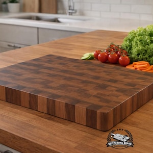 May include: A rectangular end-grain cutting board made of dark brown wood with a checkered pattern. The board features rounded corners and a thick profile. A logo with the text BEST SERVING BOARD THE GUARDIAN is visible in the bottom right corner.