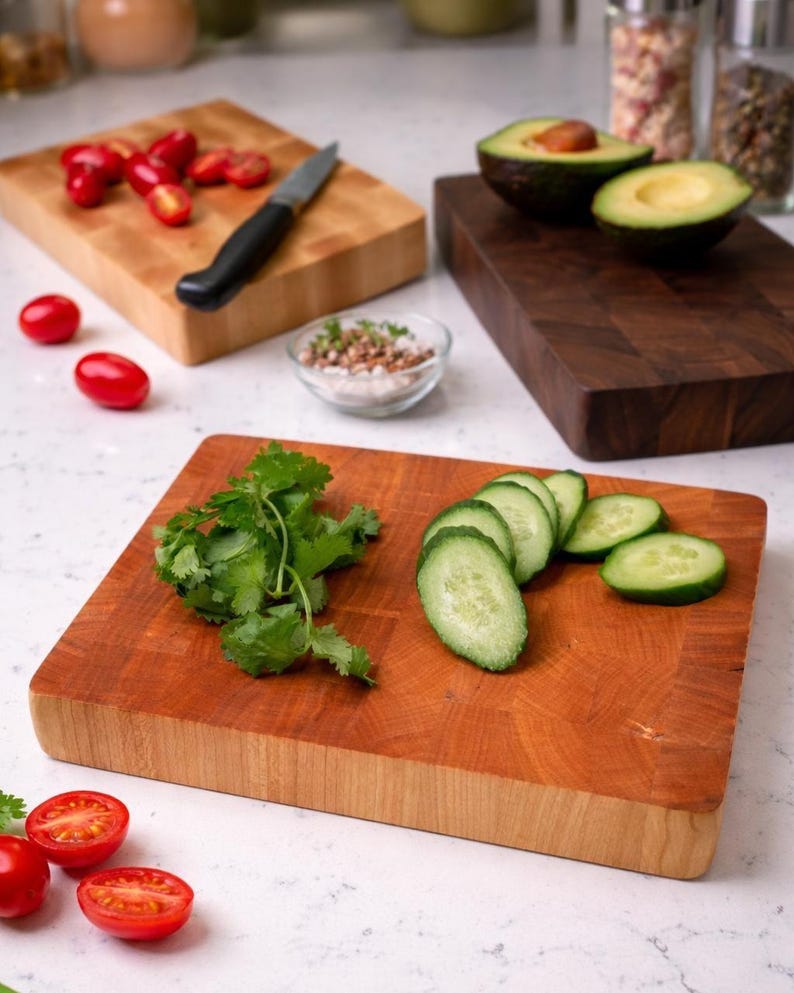 Puede incluir: Varias tablas de cortar de madera con alimentos. Una tabla tiene aguacates cortados por la mitad, otra tiene pepinos y cilantro en rodajas, y una tercera tiene tomates cherry y un cuchillo. Las tablas son de diferentes colores y tama&ntilde;os.