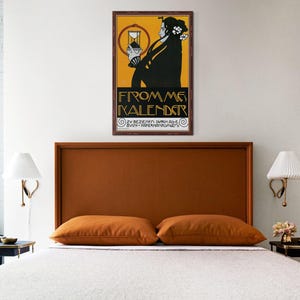May include: A bedroom with a bed featuring a brown headboard and two orange pillows. A framed vintage poster with a woman in black and the text "FROM ME KALENDER" hangs above the bed. The room has white walls and two wall-mounted lamps.