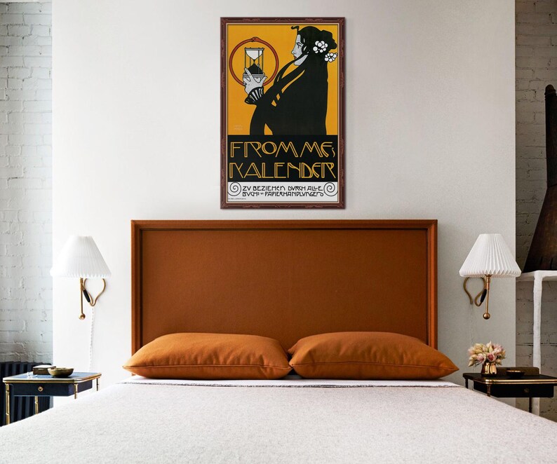 May include: A bedroom with a bed featuring a brown headboard and two orange pillows. A framed vintage poster with a woman in black and the text "FROM ME KALENDER" hangs above the bed. The room has white walls and two wall-mounted lamps.