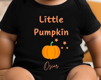May include: A baby wearing a black bodysuit with the text "Little Pumpkin" and a small orange pumpkin graphic. The text "Oscar" is written below the pumpkin. The baby is sitting on a white blanket with orange pumpkins in the background.