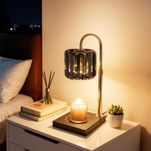 May include: A bedside table with a lit candle, a small succulent in a white pot, and a decorative lamp with a gold base and a black, faceted shade. A stack of books and a reed diffuser are also on the table.