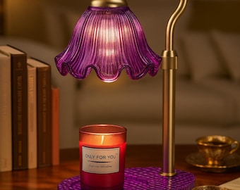 May include: A decorative table lamp with a purple glass shade and a gold-colored metal base. A red candle with the text "ONLY FOR YOU" sits on a matching purple base. The lamp is next to books and teacups.