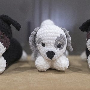Puede incluir: Tres juguetes de perro de ganchillo. Los perros están tumbados con las patas delanteras extendidas. Los perros son negros, blancos y grises. Los perros tienen narices negras y detalles marrones. Los juguetes están hechos de hilo suave.