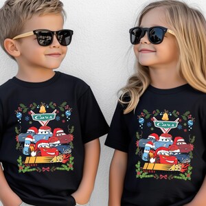 Two children wearing black t-shirts with a Cars-themed design, including characters and holiday decorations.