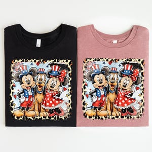 two t-shirts with a cartoon-style illustration of Mickey Mouse and Minnie Mouse wearing patriotic hats and outfits.