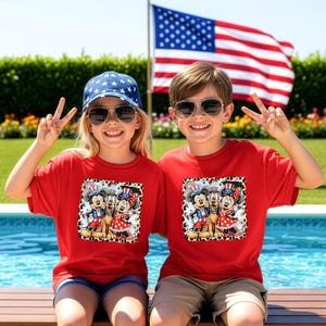 Two children wearing red t-shirts with Mickey Mouse and Minnie Mouse designs are sitting by a pool, smiling and making peace signs.