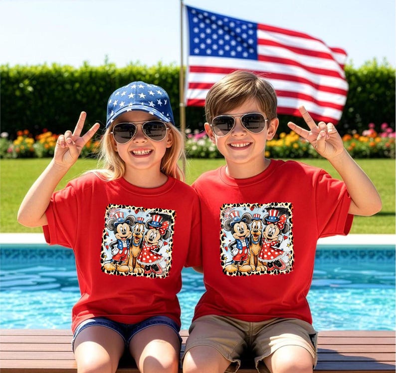 Two children wearing red t-shirts with Mickey Mouse and Minnie Mouse designs are sitting by a pool, smiling and making peace signs.