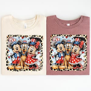 two t-shirts with a cartoon-style illustration of Mickey Mouse and Minnie Mouse, along with other Disney characters, set against a patriotic background.