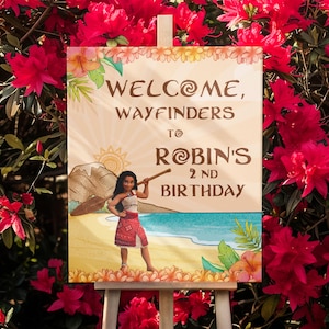 May include: A wooden sign with the words "WELCOME, WAYFINDERS TO ROBIN'S 2ND BIRTHDAY" in brown lettering. The sign features a cartoon illustration of a girl on a beach with a mountain and sun in the background. The sign is displayed on a white easel.