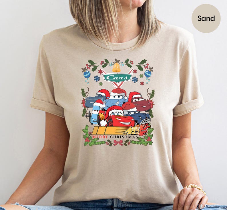 A person wearing a beige t-shirt with a Christmas-themed graphic design featuring cartoon cars and holiday decorations.