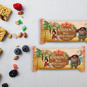May include: Two snack bar wrappers with a tropical design, featuring the text "Robin's 2nd Birthday Party." The wrappers display illustrations of characters and tropical elements, set against a light brown backdrop with orange floral borders.