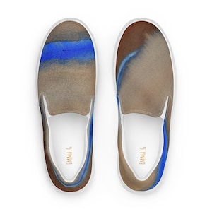 Peut inclure: Une paire de chaussures en toile blanche à enfiler avec un motif abstrait brun et bleu. Les chaussures portent le texte "EMMA.G" imprimé à l'intérieur de chaque chaussure.