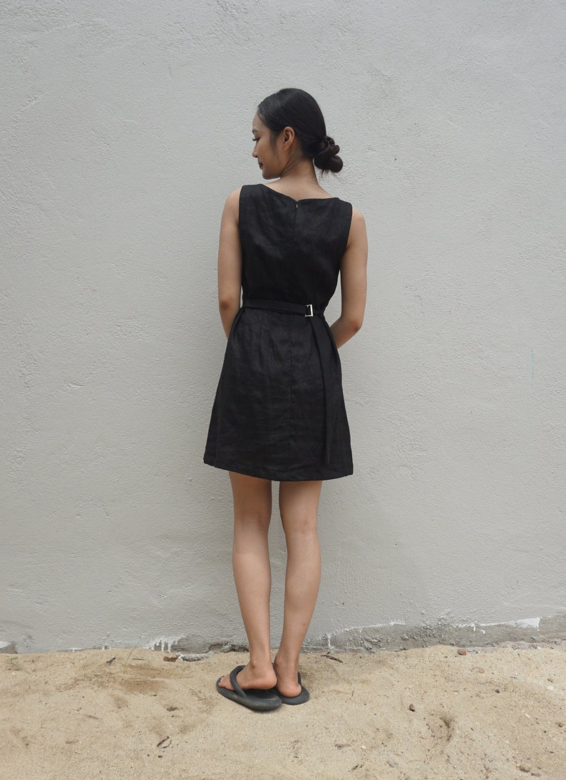 May include: A black sleeveless dress with a belt and a simple design. The dress is knee-length and has a fitted bodice.