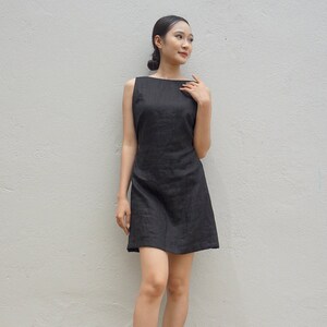 May include: A sleeveless black linen dress with a scoop neckline. The dress is fitted through the bodice and flares out slightly at the hem.