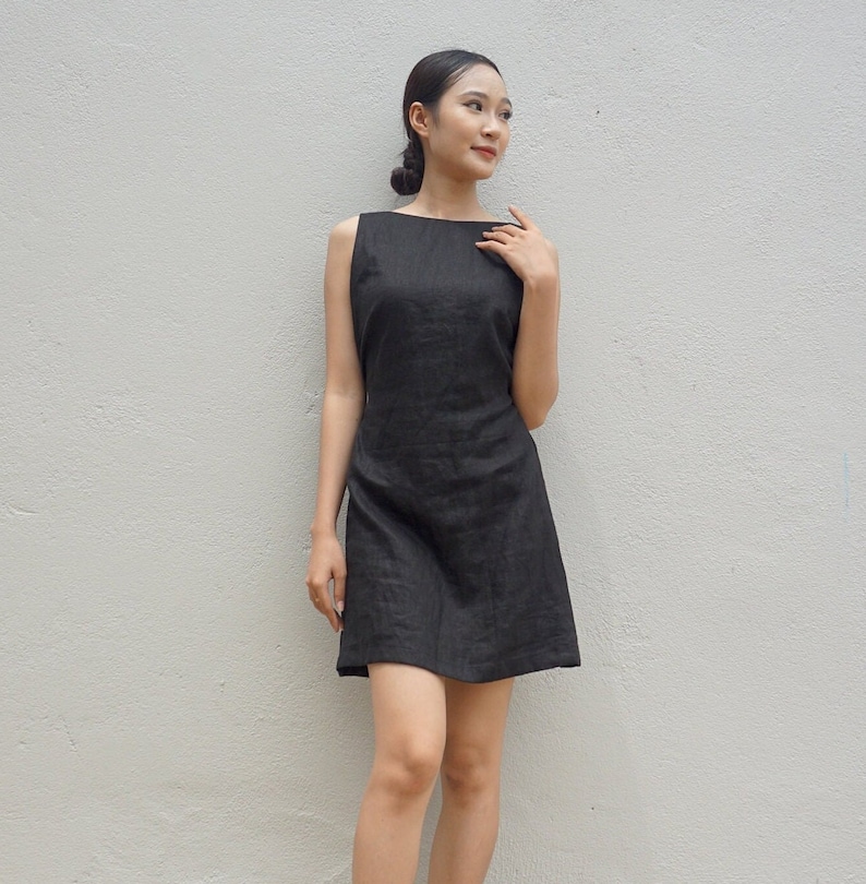 May include: A sleeveless black linen dress with a scoop neckline. The dress is fitted through the bodice and flares out slightly at the hem.