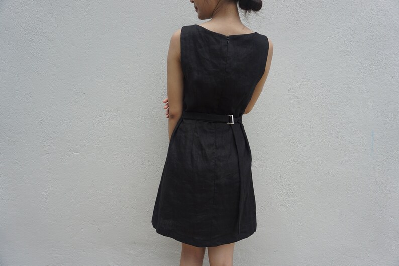 May include: A black sleeveless dress with a simple design and a belt at the waist.