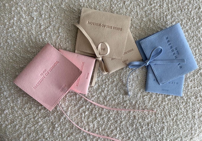 May include: Four small, fabric-covered boxes with ribbon ties. The boxes are pink, blue, and beige. The boxes are labelled "To My Matron of Honour", "To My Bridesmaid", and "Mother of the Bride".