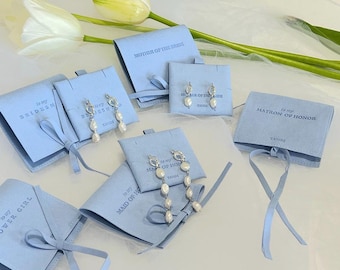 May include: Assortment of light blue gift boxes with white satin ribbon ties. Each box has a different title, such as "To my Bridesmaid", "To my Maid of Honor", and "To my Matron of Honor". Each box contains a pair of pearl earrings.